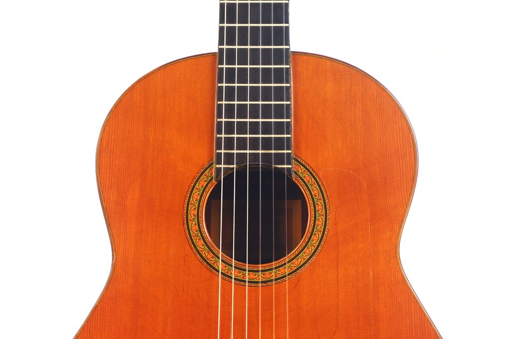 Eine Nahaufnahme einer Faustino Conde Negra Flamenco-Gitarre von Hermanos Conde aus dem Jahr 1971 hebt den hölzernen Korpus, das verschnörkelte Schallloch mit Rosette und einen Teil des Griffbretts vor einem weißen Hintergrund hervor. Eine Nahaufnahme einer Faustino Conde Negra Flamenco-Gitarre von Hermanos Conde aus dem Jahr 1971 hebt den hölzernen Korpus, das verschnörkelte Schallloch mit Rosette und einen Teil des Griffbretts vor einem weißen Hintergrund hervor.
