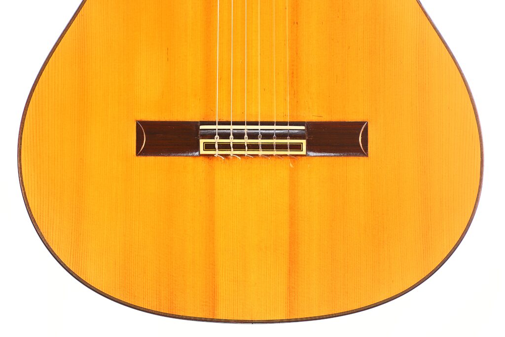 Nahaufnahme der unteren Hälfte einer Jose Ramirez 1a 1959 PB Klassische Gitarre. Hervorzuheben sind die Saiten, der Steg und der warme, polierte Holzkorpus. Nahaufnahme der unteren Hälfte einer Jose Ramirez 1a 1959 PB Klassische Gitarre. Hervorzuheben sind die Saiten, der Steg und der warme, polierte Holzkorpus.