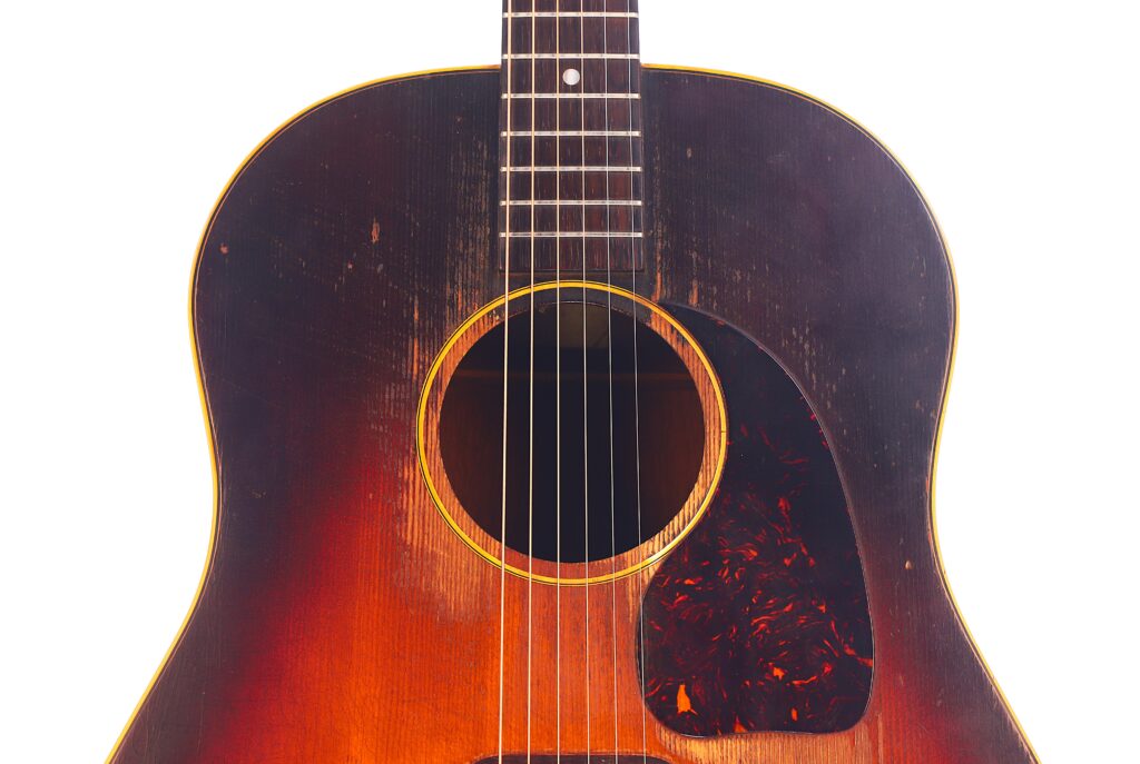 Nahaufnahme des Korpus einer abgenutzten Gibson J-45 1954 Akustische Gitarre mit sichtbaren Kratzern und einem Schildpatt-Schlagbrett vor einem weißen Hintergrund. Nahaufnahme des Korpus einer abgenutzten Gibson J-45 1954 Akustische Gitarre mit sichtbaren Kratzern und einem Schildpatt-Schlagbrett vor einem weißen Hintergrund.