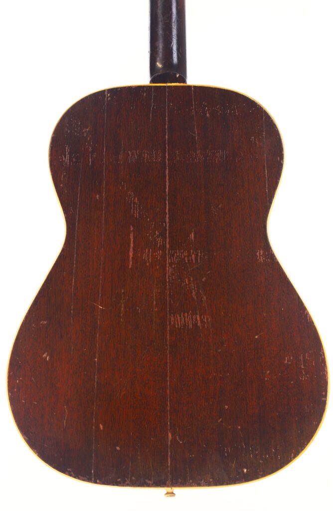 Die Rückseite der Gibson LG-1 1953 Akustik Gitarre ist aus dunklem Holz mit sichtbarer Maserung, Kratzern, einer subtilen vertikalen Naht in der Mitte, einer abgerundeten Form und gelblichen Rändern. Die Rückseite der Gibson LG-1 1953 Akustik Gitarre ist aus dunklem Holz mit sichtbarer Maserung, Kratzern, einer subtilen vertikalen Naht in der Mitte, einer abgerundeten Form und gelblichen Rändern.