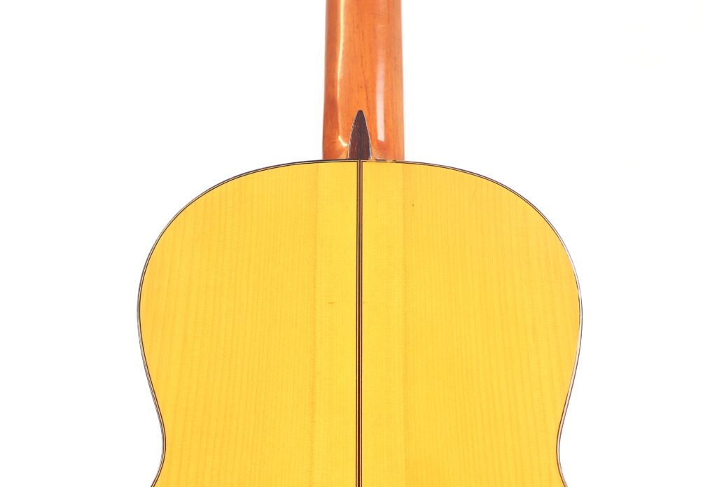 Nahaufnahme der Rückseite einer Flamenco-Gitarre von Marcelino López Nieto aus dem Jahr 1959. Sie hat einen gelben Korpus mit einem hölzernen Hals und einer zentralen dunklen Linie, die vertikal über das helle Holz verläuft. Nahaufnahme der Rückseite einer Flamenco-Gitarre von Marcelino López Nieto aus dem Jahr 1959. Sie hat einen gelben Korpus mit einem hölzernen Hals und einer zentralen dunklen Linie, die vertikal über das helle Holz verläuft.
