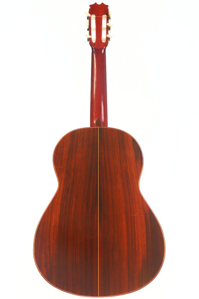 Das Bild zeigt die Rückseite einer Hermanos Conde 1971 Faustino Conde Negra Flamenco-Gitarre aus poliertem dunklem Holz mit einer zentralen Einlegearbeit. Der Hals, die Kopfplatte und die Stimmwirbel sind vor einem weißen Hintergrund sichtbar. Das Bild zeigt die Rückseite einer Hermanos Conde 1971 Faustino Conde Negra Flamenco-Gitarre aus poliertem dunklem Holz mit einer zentralen Einlegearbeit. Der Hals, die Kopfplatte und die Stimmwirbel sind vor einem weißen Hintergrund sichtbar.