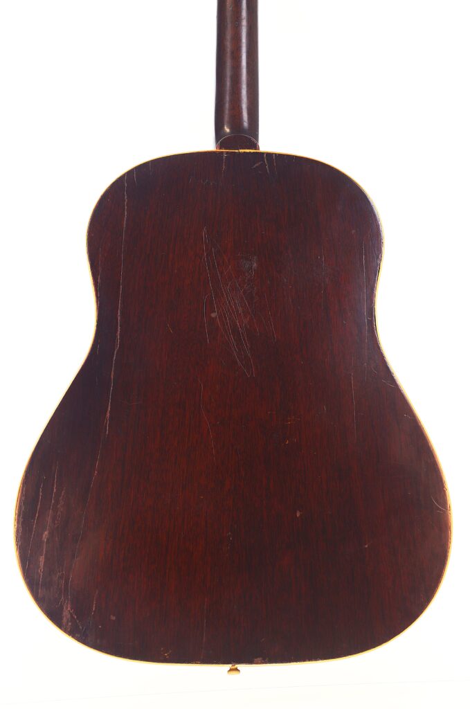 Das Bild zeigt die Rückseite einer Gibson J-45 1954 Akustische Gitarre mit dunklem Holzfinish, sichtbaren Kratzern, Abnutzungserscheinungen an den Kanten und dem oben sichtbaren Hals. Das Bild zeigt die Rückseite einer Gibson J-45 1954 Akustische Gitarre mit dunklem Holzfinish, sichtbaren Kratzern, Abnutzungserscheinungen an den Kanten und dem oben sichtbaren Hals.