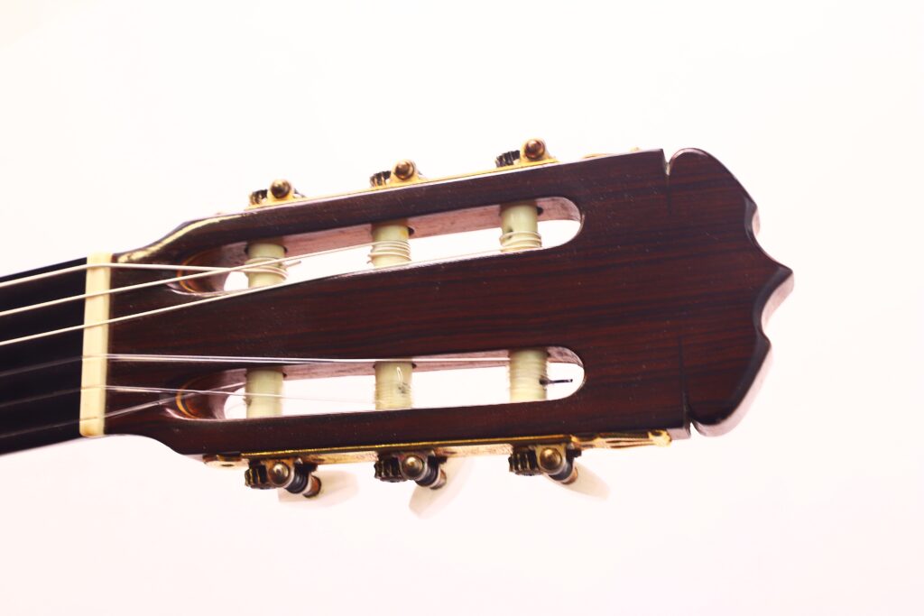 Nahaufnahme der Kopfplatte einer Jose Ramirez 1a 1959 PB Klassische Gitarre mit Stimmwirbeln, Saiten und einer dunklen Holzoberfläche vor einem schlichten weißen Hintergrund. Nahaufnahme der Kopfplatte einer Jose Ramirez 1a 1959 PB Klassische Gitarre mit Stimmwirbeln, Saiten und einer dunklen Holzoberfläche vor einem schlichten weißen Hintergrund.