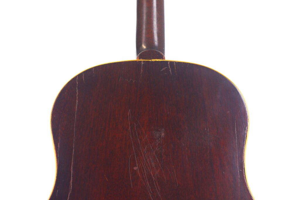 Nahaufnahme der Rückseite einer Gibson J-45 1954 Akustische Gitarre, die dunkles Holz mit sichtbaren Kratzern und einer gelben Kontur entlang der Kante aufweist, fotografiert vor einem weißen Hintergrund. Nahaufnahme der Rückseite einer Gibson J-45 1954 Akustische Gitarre, die dunkles Holz mit sichtbaren Kratzern und einer gelben Kontur entlang der Kante aufweist, fotografiert vor einem weißen Hintergrund.