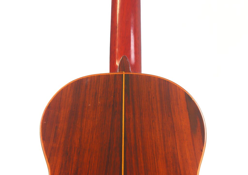 Nahaufnahme der Rückseite und des Halses einer Faustino Conde Negra Flamenco-Gitarre von Hermanos Conde aus dem Jahr 1971. Hervorzuheben sind die polierte Maserung des dunklen Holzes und die gelbe Verzierung vor einem weißen Hintergrund. Nahaufnahme der Rückseite und des Halses einer Faustino Conde Negra Flamenco-Gitarre von Hermanos Conde aus dem Jahr 1971. Hervorzuheben sind die polierte Maserung des dunklen Holzes und die gelbe Verzierung vor einem weißen Hintergrund.