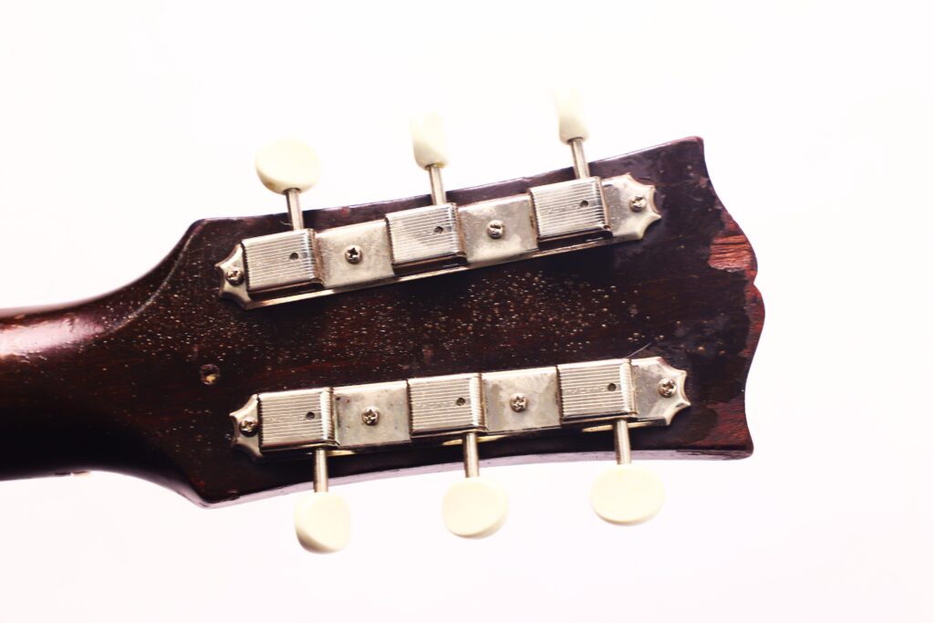 Nahaufnahme der Rückseite der Gibson LG-1 1953 Akustik Gitarre mit den Metallmechaniken und der dunklen Holzoberfläche vor weißem Hintergrund. Nahaufnahme der Rückseite der Gibson LG-1 1953 Akustik Gitarre mit den Metallmechaniken und der dunklen Holzoberfläche vor weißem Hintergrund.