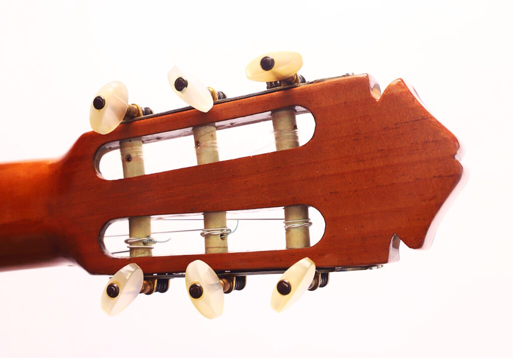 Nahaufnahme der Kopfplatte einer Flamenco-Gitarre von Marcelino López Nieto aus dem Jahr 1959 mit sechs Stimmwirbeln und Nylonsaiten vor weißem Hintergrund. Nahaufnahme der Kopfplatte einer Flamenco-Gitarre von Marcelino López Nieto aus dem Jahr 1959 mit sechs Stimmwirbeln und Nylonsaiten vor weißem Hintergrund.