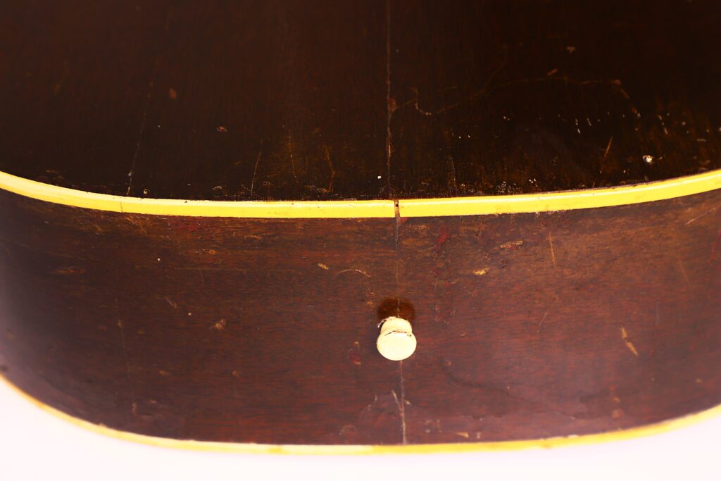 Nahaufnahme der Seite einer Gibson LG-1 1953 Akustik-Gitarre mit gelblichem Binding, einem zentralen weißen Gurtknopf und sichtbaren Kratzern, die ihren Vintage-Charme unterstreichen. Nahaufnahme der Seite einer Gibson LG-1 1953 Akustik-Gitarre mit gelblichem Binding, einem zentralen weißen Gurtknopf und sichtbaren Kratzern, die ihren Vintage-Charme unterstreichen.