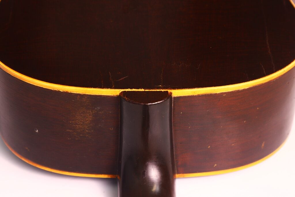 Nahaufnahme von Boden und Hals einer Gibson J-45 1954 Akustische Gitarre mit dunkelbraunem Finish, gelbem Binding entlang der Kanten und sichtbaren Gebrauchsspuren. Nahaufnahme von Boden und Hals einer Gibson J-45 1954 Akustische Gitarre mit dunkelbraunem Finish, gelbem Binding entlang der Kanten und sichtbaren Gebrauchsspuren.