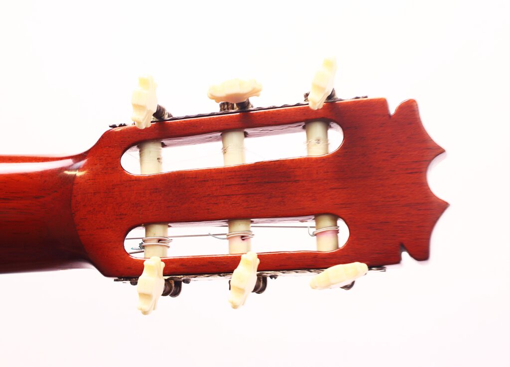 Nahaufnahme der Kopfplatte einer Faustino Conde Negra Flamenco-Gitarre von Hermanos Conde aus dem Jahr 1971 mit cremefarbenen Stimmwirbeln und sichtbarem Holzfinish vor weißem Hintergrund. Nahaufnahme der Kopfplatte einer Faustino Conde Negra Flamenco-Gitarre von Hermanos Conde aus dem Jahr 1971 mit cremefarbenen Stimmwirbeln und sichtbarem Holzfinish vor weißem Hintergrund.