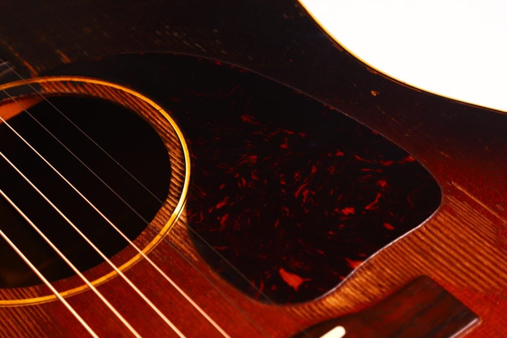 Nahaufnahme der Gibson J-45 1954 Akustische Gitarre, die das Schallloch, die Saiten, einen Teil des Schlagbretts und den reichhaltig verarbeiteten dunklen Holzkorpus zeigt. Nahaufnahme der Gibson J-45 1954 Akustische Gitarre, die das Schallloch, die Saiten, einen Teil des Schlagbretts und den reichhaltig verarbeiteten dunklen Holzkorpus zeigt.