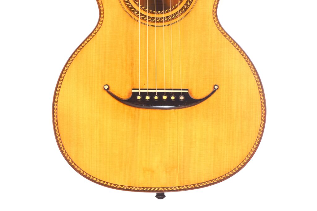 Nahaufnahme des unteren Korpus der Marc Antonio Romantikgitarre, mit hellem Holzfinish, dekorativer Randeinlage, sechs Saiten und schwarzem Steg. Nahaufnahme des unteren Korpus der Marc Antonio Romantikgitarre, mit hellem Holzfinish, dekorativer Randeinlage, sechs Saiten und schwarzem Steg.