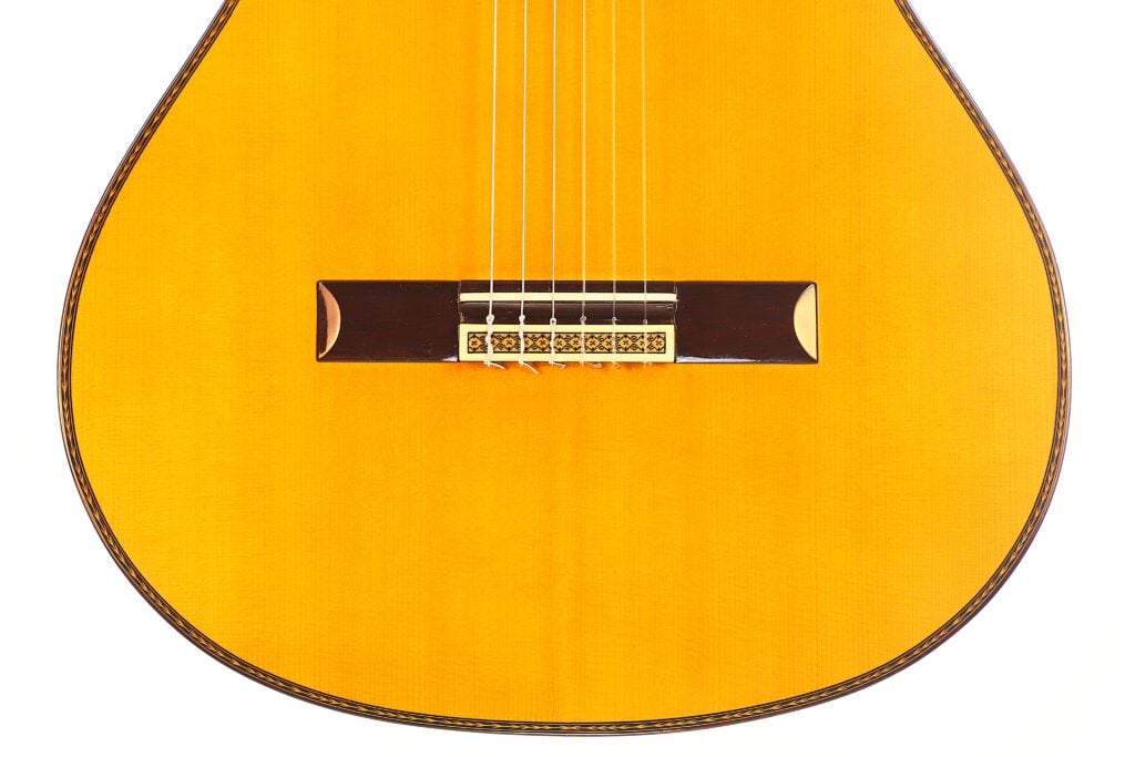 Nahaufnahme der Manuel Contreras Double Top 1985 Klassische Gitarre. Hervorzuheben sind die Saiten, der Steg und die warme natürliche Holzoberfläche. Das Bild konzentriert sich auf die untere Hälfte dieser klassischen Gitarre. Nahaufnahme der Manuel Contreras Double Top 1985 Klassische Gitarre. Hervorzuheben sind die Saiten, der Steg und die warme natürliche Holzoberfläche. Das Bild konzentriert sich auf die untere Hälfte dieser klassischen Gitarre.
