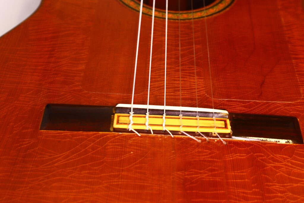 Nahaufnahme der Saiten und des Stegs einer Faustino Conde Negra Flamenco-Gitarre von Hermanos Conde aus dem Jahr 1971, die die Maserung des Holzes und die handwerklichen Details der Oberfläche hervorhebt. Nahaufnahme der Saiten und des Stegs einer Faustino Conde Negra Flamenco-Gitarre von Hermanos Conde aus dem Jahr 1971, die die Maserung des Holzes und die handwerklichen Details der Oberfläche hervorhebt.