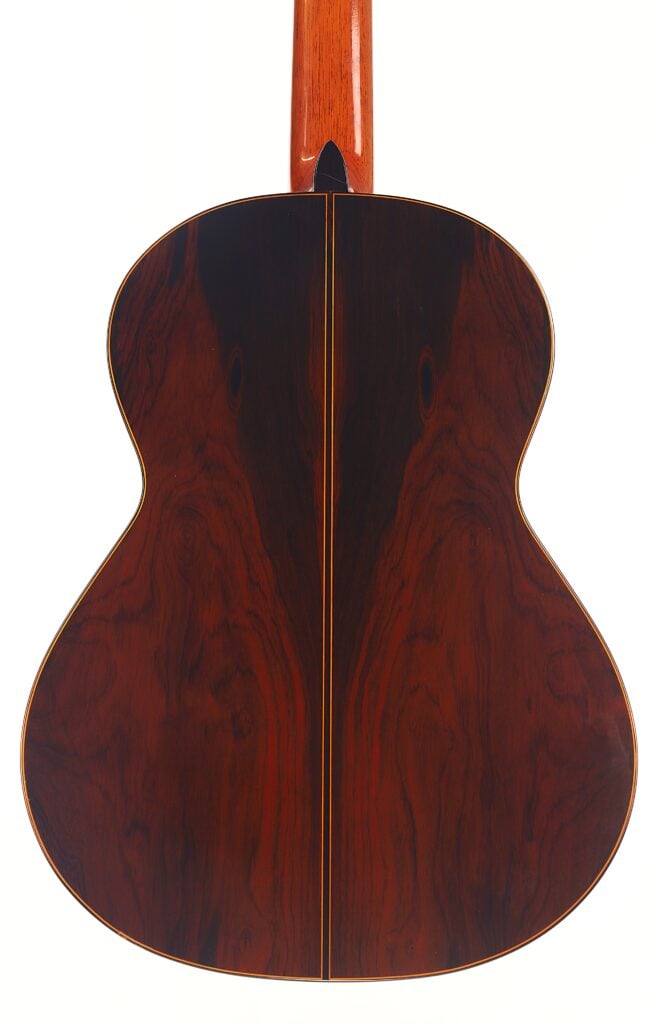 Die Manuel Contreras Double Top 1985 Klassische Gitarre hat einen Boden aus dunklem, poliertem Holz mit sichtbarer Maserung und einer zentralen Naht, die auf einem Foto vor weißem Hintergrund zu sehen ist. Die Manuel Contreras Double Top 1985 Klassische Gitarre hat einen Boden aus dunklem, poliertem Holz mit sichtbarer Maserung und einer zentralen Naht, die auf einem Foto vor weißem Hintergrund zu sehen ist.