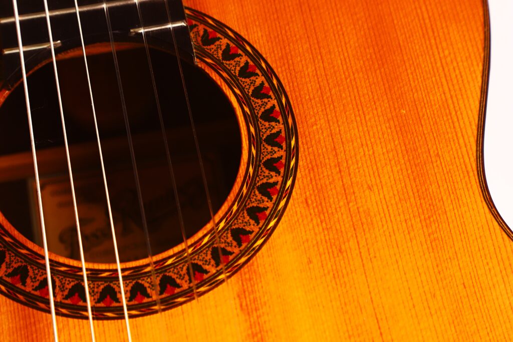 Nahaufnahme des Schalllochs der Jose Ramirez 1a 1959 PB Klassische Gitarre. Hervorzuheben sind die rot-schwarze Rosette, die sichtbaren Saiten und die warme Holzmaserung des Korpus. Nahaufnahme des Schalllochs der Jose Ramirez 1a 1959 PB Klassische Gitarre. Hervorzuheben sind die rot-schwarze Rosette, die sichtbaren Saiten und die warme Holzmaserung des Korpus.