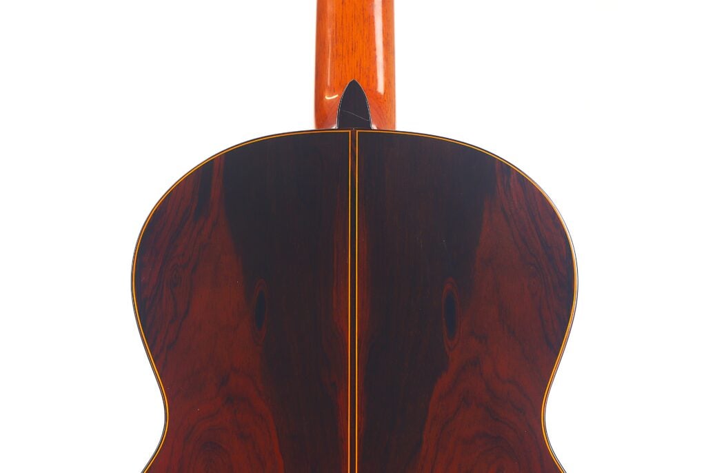 Nahaufnahme der Rückseite der Manuel Contreras Double Top 1985 Klassische Gitarre mit glänzendem dunklem Holz mit sichtbarer Maserung und einem schmalen hellen Streifen in der Mitte. Nahaufnahme der Rückseite der Manuel Contreras Double Top 1985 Klassische Gitarre mit glänzendem dunklem Holz mit sichtbarer Maserung und einem schmalen hellen Streifen in der Mitte.