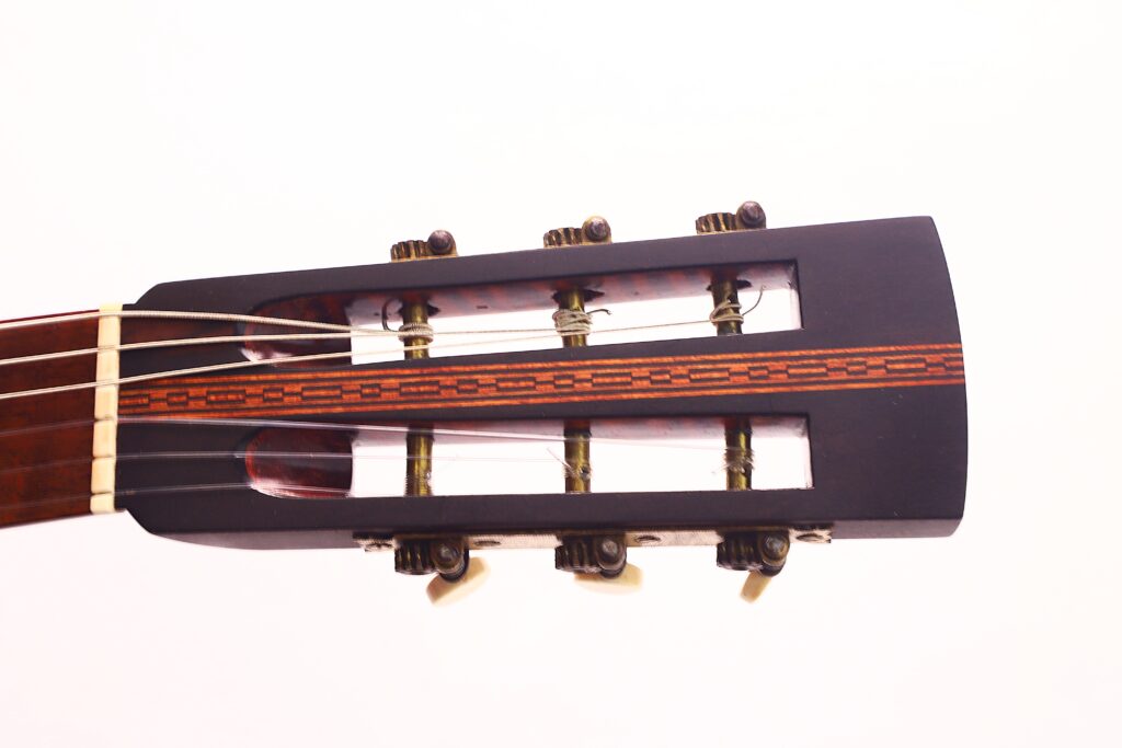 Nahaufnahme der Kopfplatte der Marc Antonio Romantikgitarre mit sechs Stimmwirbeln (drei pro Seite) und dekorativer Einlage, dargestellt vor einem schlichten weißen Hintergrund. Nahaufnahme der Kopfplatte der Marc Antonio Romantikgitarre mit sechs Stimmwirbeln (drei pro Seite) und dekorativer Einlage, dargestellt vor einem schlichten weißen Hintergrund.