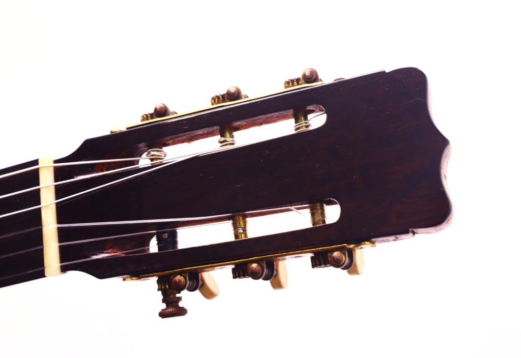 Nahaufnahme der Kopfplatte der Klassischen Gitarre von Juan Lopez Jimenez aus dem Jahr 1933 mit Stimmwirbeln, Sattel und Saiten vor weißem Hintergrund. Nahaufnahme der Kopfplatte der Klassischen Gitarre von Juan Lopez Jimenez aus dem Jahr 1933 mit Stimmwirbeln, Sattel und Saiten vor weißem Hintergrund.