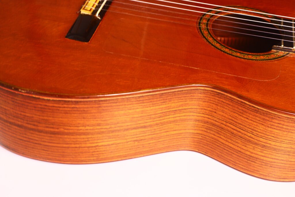 Nahaufnahme des Korpus der Hermanos Conde 1971 Faustino Conde Negra Flamenco-Gitarre, wobei die Holzmaserung, die Saiten, das Schallloch und der Steg vor einem weißen Hintergrund hervorgehoben werden. Nahaufnahme des Korpus der Hermanos Conde 1971 Faustino Conde Negra Flamenco-Gitarre, wobei die Holzmaserung, die Saiten, das Schallloch und der Steg vor einem weißen Hintergrund hervorgehoben werden.