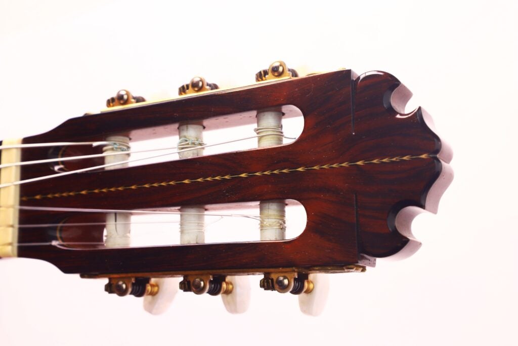 Nahaufnahme der Kopfplatte der Manuel Contreras Double Top 1985 Klassische Gitarre, mit hölzernen Stimmwirbeln, Saiten und feiner Handwerkskunst vor einem schlichten weißen Hintergrund. Nahaufnahme der Kopfplatte der Manuel Contreras Double Top 1985 Klassische Gitarre, mit hölzernen Stimmwirbeln, Saiten und feiner Handwerkskunst vor einem schlichten weißen Hintergrund.