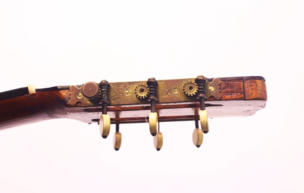 Nahaufnahme der Stimmwirbel und Zahnräder an der Kopfplatte einer Juan Lopez Jimenez 1933 Klassische Gitarre, die das abgenutzte Holz und die Messingbeschläge vor einem schlichten weißen Hintergrund hervorhebt. Nahaufnahme der Stimmwirbel und Zahnräder an der Kopfplatte einer Juan Lopez Jimenez 1933 Klassische Gitarre, die das abgenutzte Holz und die Messingbeschläge vor einem schlichten weißen Hintergrund hervorhebt.