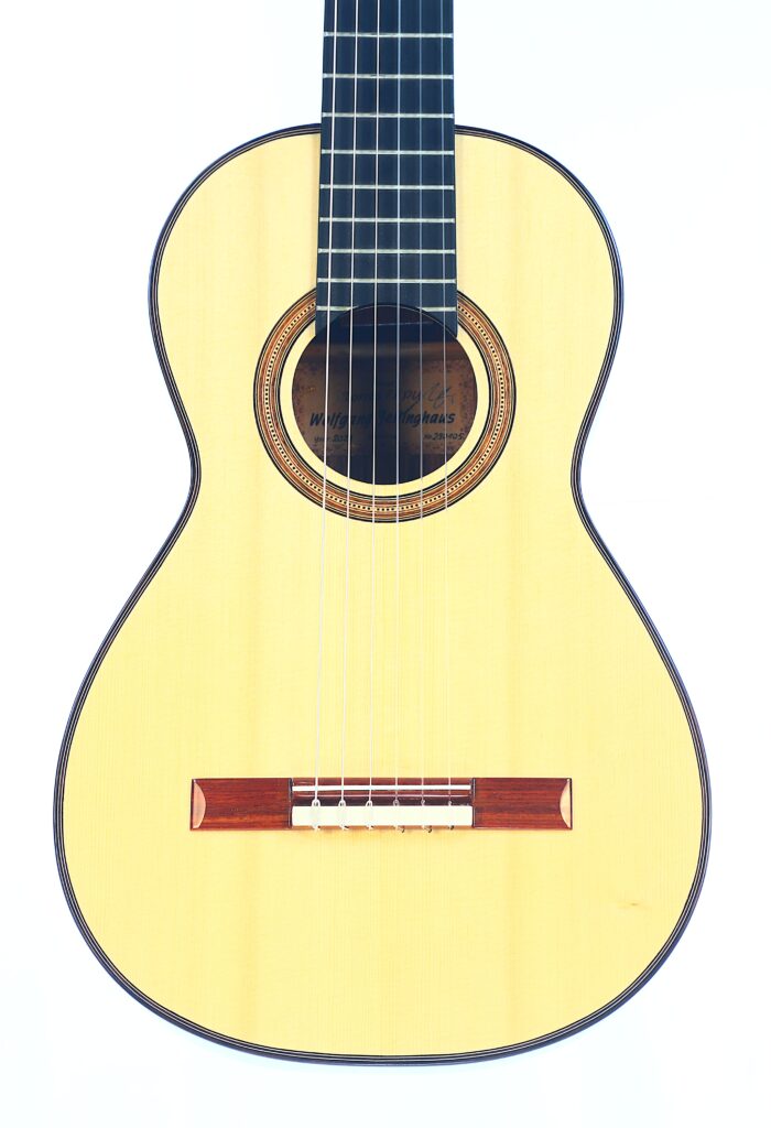 Die Jellinghaus Torres 77 PU Klassische Gitarre ist eine klassische Akustikgitarre mit einem hellen Holzkorpus, dunklem Griffbrett, sechs Saiten und einer dekorativen Rosette um das Schallloch auf weißem Grund. Die Jellinghaus Torres 77 PU Klassische Gitarre ist eine klassische Akustikgitarre mit einem hellen Holzkorpus, dunklem Griffbrett, sechs Saiten und einer dekorativen Rosette um das Schallloch auf weißem Grund.