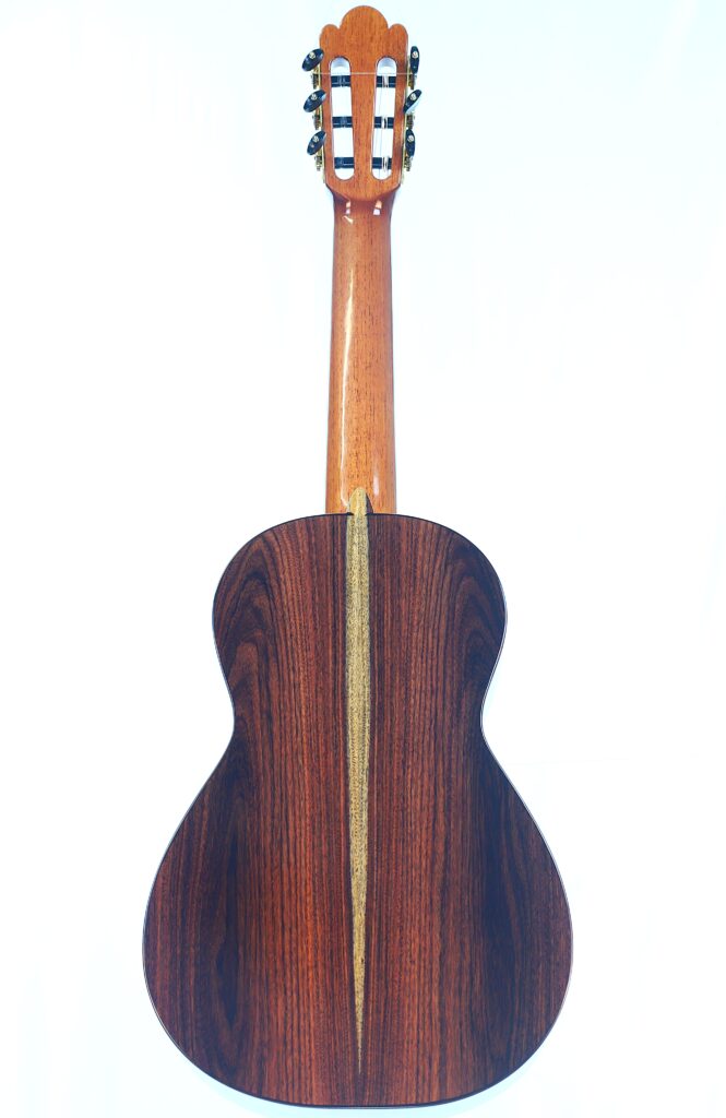 Die Abbildung zeigt die Rückseite der Jellinghaus Torres 77 PU Klassische Gitarre, die einen dunklen Holzkorpus mit einem helleren vertikalen Mittelstreifen und einem helleren Hals aufweist. Die Abbildung zeigt die Rückseite der Jellinghaus Torres 77 PU Klassische Gitarre, die einen dunklen Holzkorpus mit einem helleren vertikalen Mittelstreifen und einem helleren Hals aufweist.