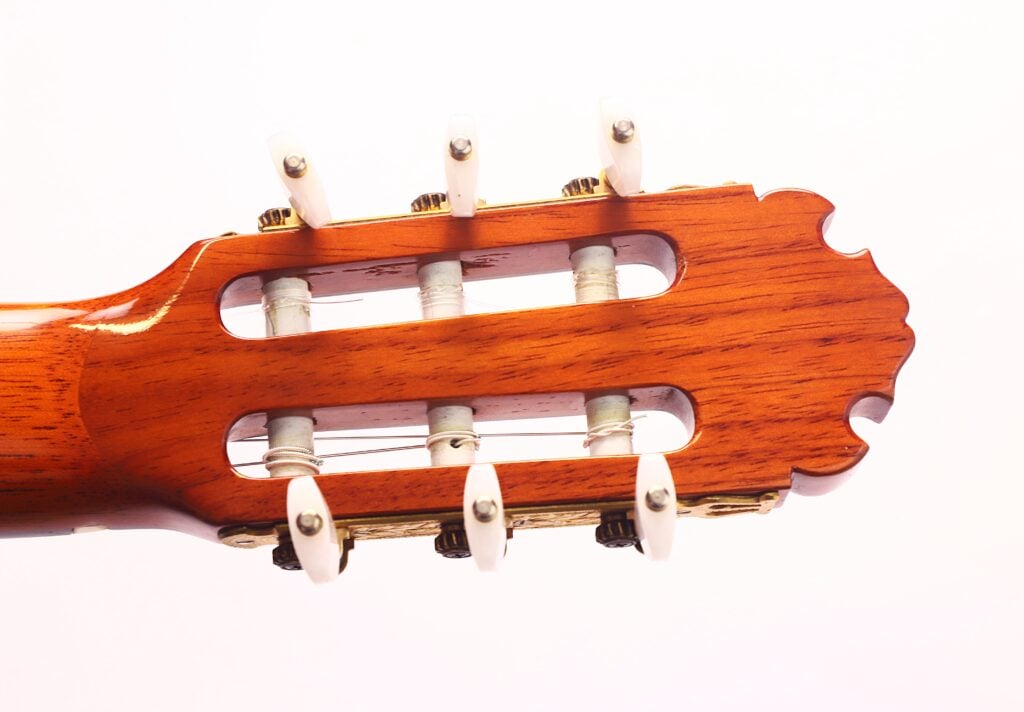 Nahaufnahme der Kopfplatte der Manuel Contreras Double Top 1985 Klassische Gitarre mit hölzerner Oberfläche, weißen Stimmwirbeln und silbernen Stimmmechaniken vor einem schlichten weißen Hintergrund. Nahaufnahme der Kopfplatte der Manuel Contreras Double Top 1985 Klassische Gitarre mit hölzerner Oberfläche, weißen Stimmwirbeln und silbernen Stimmmechaniken vor einem schlichten weißen Hintergrund.