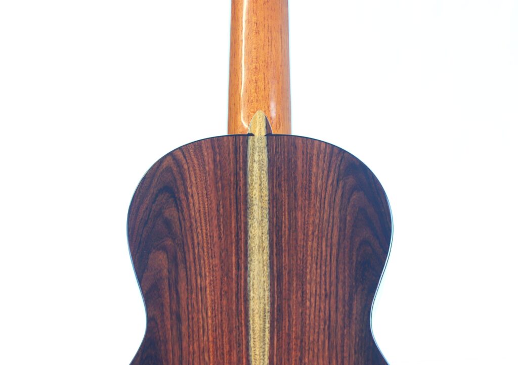 Nahaufnahme des Bodens der Jellinghaus Torres 77 PU Klassische Gitarre mit einer polierten Holzoberfläche mit Mittelstreifen und sichtbaren Maserungen. Der Gitarrenhals ragt vor weißem Hintergrund aus dem Korpus heraus. Nahaufnahme des Bodens der Jellinghaus Torres 77 PU Klassische Gitarre mit einer polierten Holzoberfläche mit Mittelstreifen und sichtbaren Maserungen. Der Gitarrenhals ragt vor weißem Hintergrund aus dem Korpus heraus.