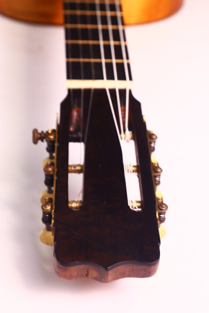 Nahaufnahme der Kopfplatte der Juan Lopez Jimenez 1933 Klassische Gitarre, die Stimmwirbel, Saiten und Hals vor einem hellen Hintergrund zeigt. Das Holz hat eine satte dunkle Oberfläche mit sichtbaren Metallmechaniken auf beiden Seiten. Nahaufnahme der Kopfplatte der Juan Lopez Jimenez 1933 Klassische Gitarre, die Stimmwirbel, Saiten und Hals vor einem hellen Hintergrund zeigt. Das Holz hat eine satte dunkle Oberfläche mit sichtbaren Metallmechaniken auf beiden Seiten.