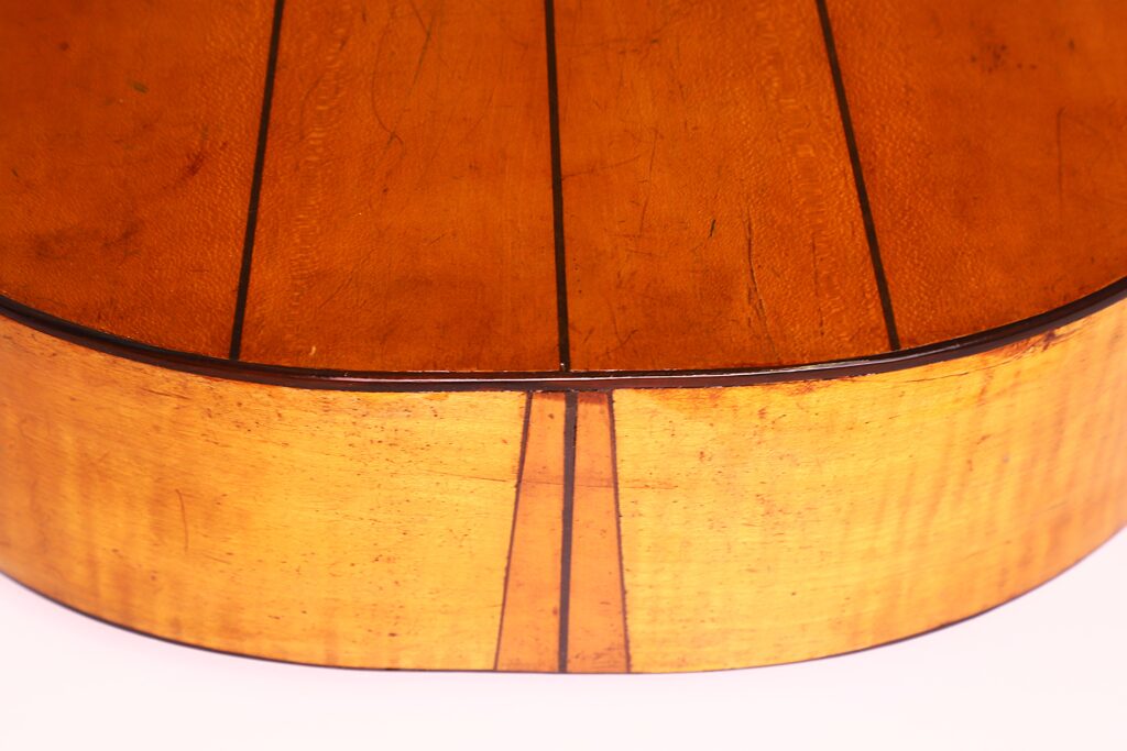 Nahaufnahme der Rückseite und des Randes einer Juan Lopez Jimenez Klassische Gitarre von 1933 mit ihrer glatten, polierten Holzmaserung und den dunklen Einlegearbeiten vor weißem Hintergrund. Nahaufnahme der Rückseite und des Randes einer Juan Lopez Jimenez Klassische Gitarre von 1933 mit ihrer glatten, polierten Holzmaserung und den dunklen Einlegearbeiten vor weißem Hintergrund.