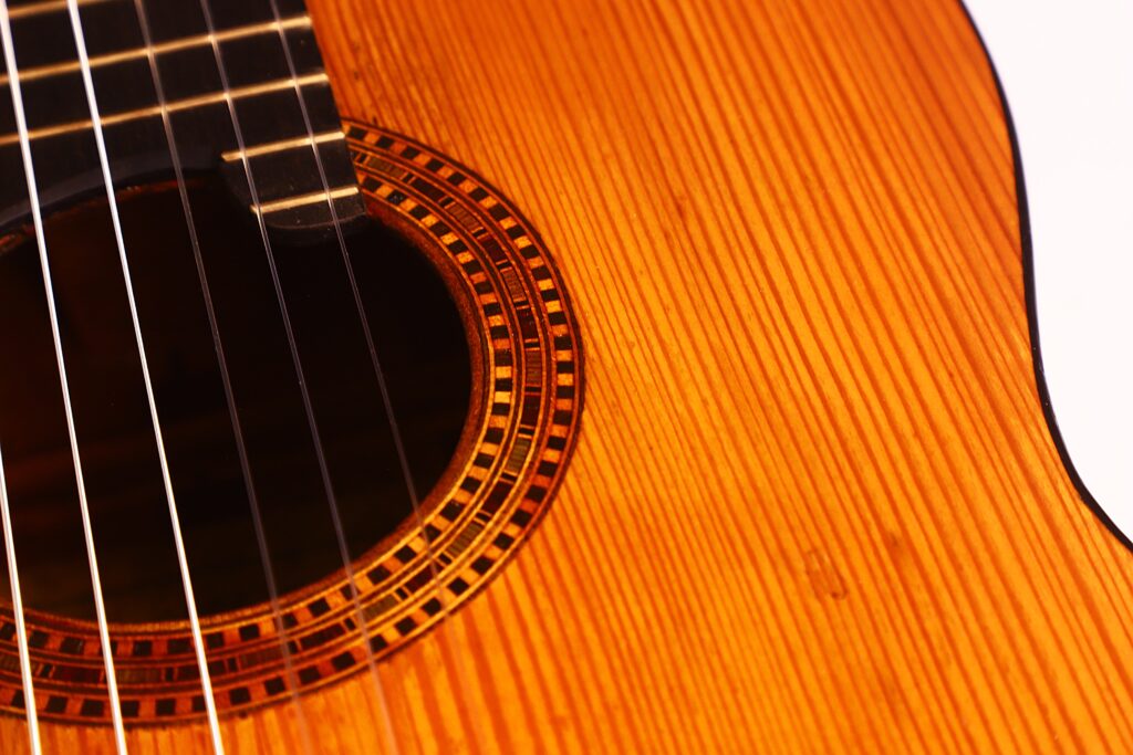 Nahaufnahme der Juan Lopez Jimenez 1933 Klassische Gitarre, die die Holzstruktur, das Schallloch mit der dekorativen Rosette und die Gitarrensaiten hervorhebt, um die detaillierte Handwerkskunst des Instruments zu zeigen. Nahaufnahme der Juan Lopez Jimenez 1933 Klassische Gitarre, die die Holzstruktur, das Schallloch mit der dekorativen Rosette und die Gitarrensaiten hervorhebt, um die detaillierte Handwerkskunst des Instruments zu zeigen.