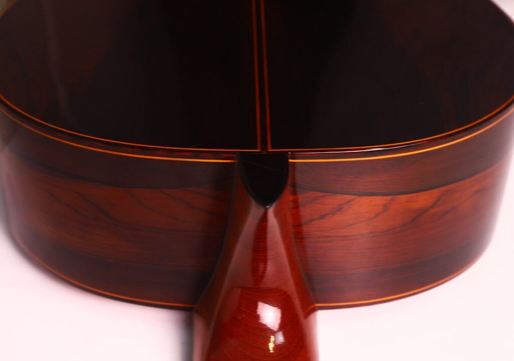Nahaufnahme des Bodens und des Halses der Manuel Contreras Double Top 1985 Klassische Gitarre. Hervorzuheben sind die reiche braune Holzmaserung, die glänzende Oberfläche und die feinen handwerklichen Details. Nahaufnahme des Bodens und des Halses der Manuel Contreras Double Top 1985 Klassische Gitarre. Hervorzuheben sind die reiche braune Holzmaserung, die glänzende Oberfläche und die feinen handwerklichen Details.