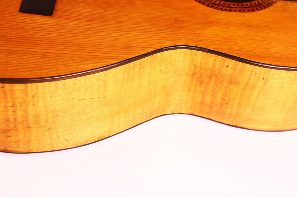Nahaufnahme der Seite und des unteren Korpus der Juan Lopez Jimenez 1933 Klassische Gitarre, wobei die natürliche Holzoberfläche, die Maserung und die Kurven vor einem weißen Hintergrund zu sehen sind. Nahaufnahme der Seite und des unteren Korpus der Juan Lopez Jimenez 1933 Klassische Gitarre, wobei die natürliche Holzoberfläche, die Maserung und die Kurven vor einem weißen Hintergrund zu sehen sind.