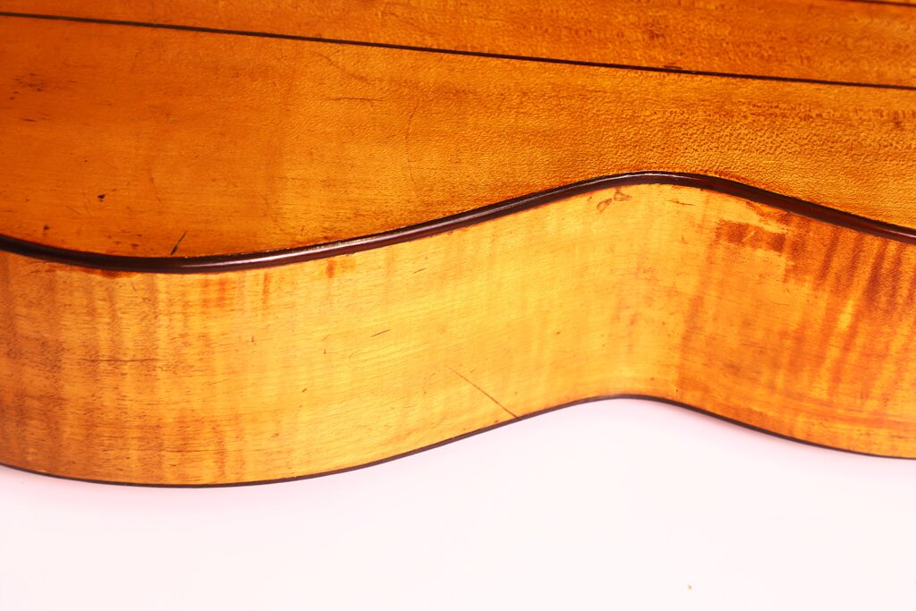 Nahaufnahme der Seite einer Juan Lopez Jimenez 1933 Klassische Gitarre, die die Holzmaserung, die glatte Oberfläche und die natürlichen Variationen vor einem weißen Hintergrund hervorhebt. Nahaufnahme der Seite einer Juan Lopez Jimenez 1933 Klassische Gitarre, die die Holzmaserung, die glatte Oberfläche und die natürlichen Variationen vor einem weißen Hintergrund hervorhebt.