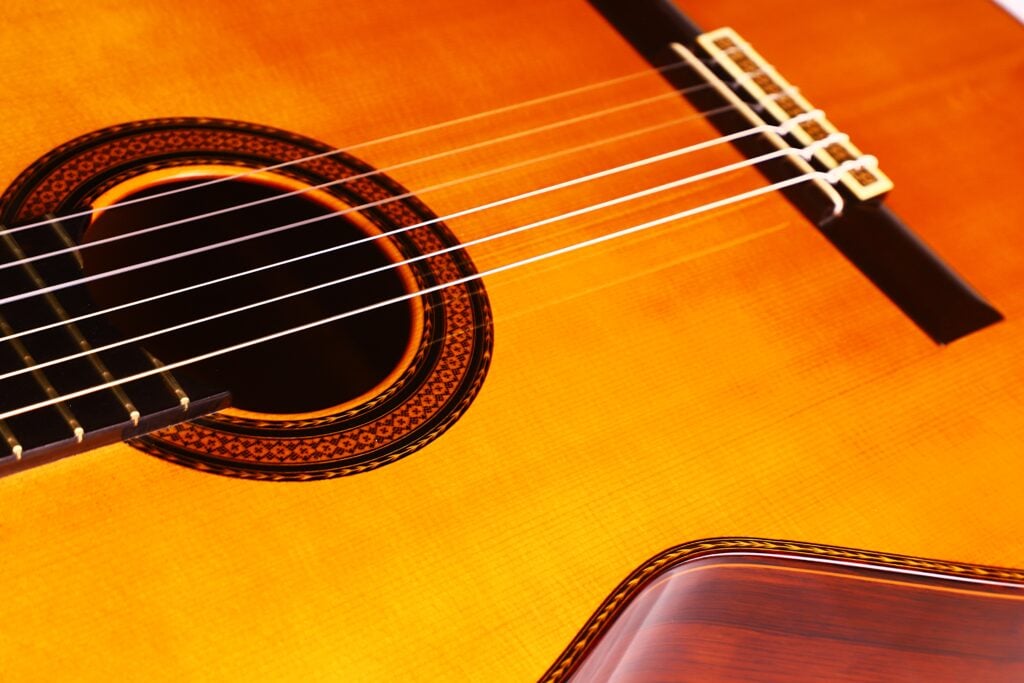 Nahaufnahme der Manuel Contreras Double Top 1985 Klassische Gitarre. Hervorzuheben sind die Saiten, die Zierrosette um das Schallloch und der warme, glänzende Holzkorpus. Nahaufnahme der Manuel Contreras Double Top 1985 Klassische Gitarre. Hervorzuheben sind die Saiten, die Zierrosette um das Schallloch und der warme, glänzende Holzkorpus.