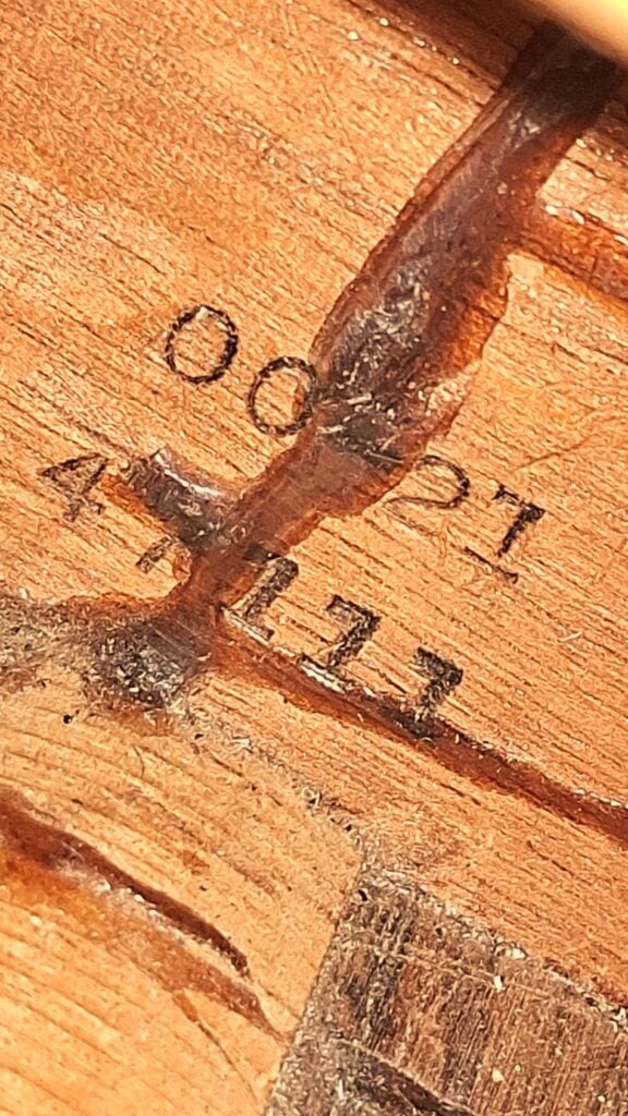Nahaufnahme der Holzoberfläche der Martin 00-21 1931 Akustik Gitarre mit dunklen, rauen Rissen und den eingravierten Nummern 00221 und 4113. Die Beleuchtung hebt die Holztextur und -maserung der Gitarre hervor. Nahaufnahme der Holzoberfläche der Martin 00-21 1931 Akustik Gitarre mit dunklen, rauen Rissen und den eingravierten Nummern 00221 und 4113. Die Beleuchtung hebt die Holztextur und -maserung der Gitarre hervor.