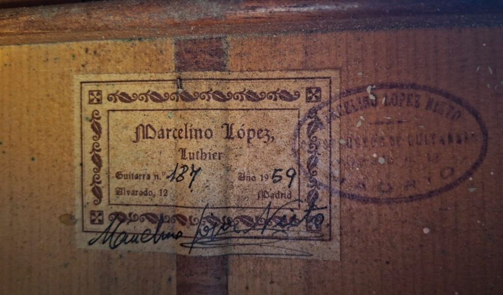 Nahaufnahme eines Gitarrenetiketts mit der Aufschrift "Marcelino López, Geigenbauer" und handschriftlichen Angaben: "Guitarra No 187, Año 1959, Madrid". Sichtbar sind Stempel, Unterschrift und Holzmaserung auf dieser Marcelino López Nieto 1959 Flamenco Gitarre. Nahaufnahme eines Gitarrenetiketts mit der Aufschrift "Marcelino López, Geigenbauer" und handschriftlichen Angaben: "Guitarra No 187, Año 1959, Madrid". Sichtbar sind Stempel, Unterschrift und Holzmaserung auf dieser Marcelino López Nieto 1959 Flamenco Gitarre.