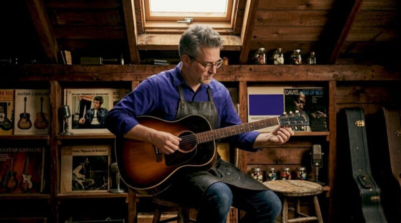 Collector examining vintage Gibson guitar in wood-paneled study