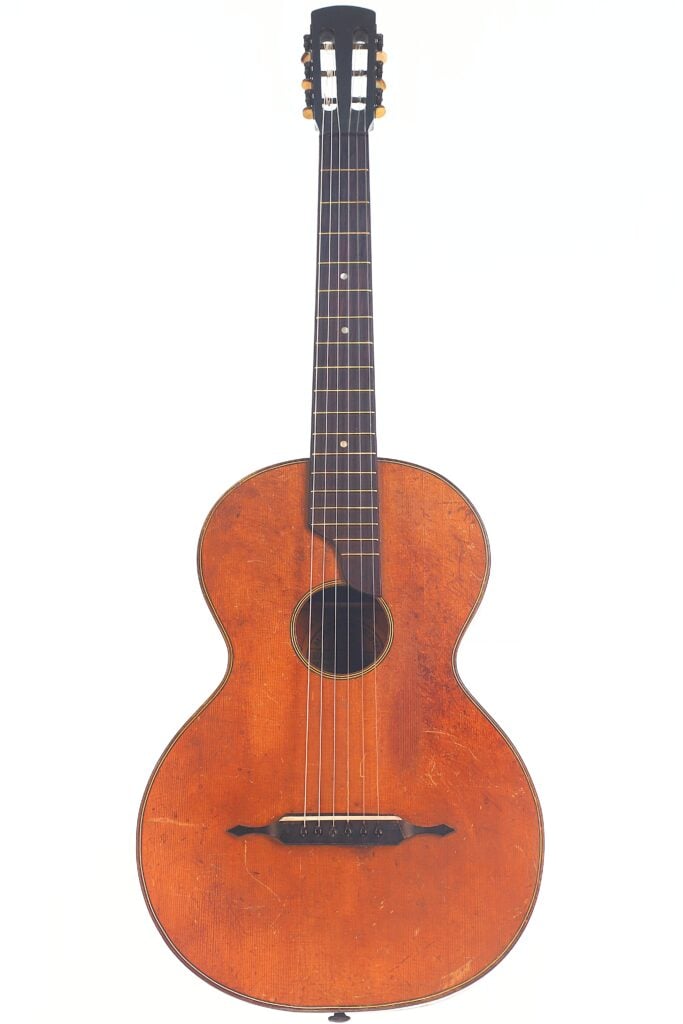 Die Braun & Hauser 1905 Klassische Gitarre ist eine historische Akustikgitarre mit Holzkorpus, dunklem Griffbrett und sechs Saiten, die aufrecht vor einem schlichten weißen Hintergrund steht. Die Braun & Hauser 1905 Klassische Gitarre ist eine historische Akustikgitarre mit Holzkorpus, dunklem Griffbrett und sechs Saiten, die aufrecht vor einem schlichten weißen Hintergrund steht.
