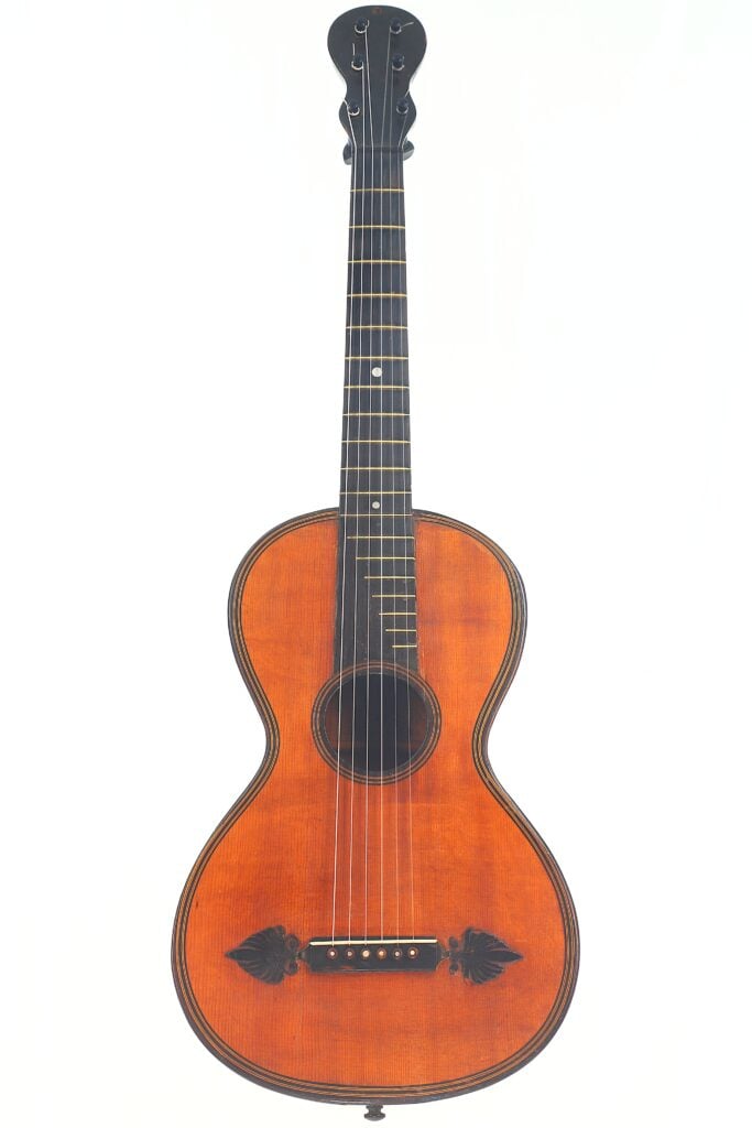 Die Stephan Thumhart 1838 Romantikgitarre ist eine Vintage-Akustikgitarre mit einem Griffbrett aus dunklem Holz, sechs Saiten, dekorativen Verzierungen am Korpus und einer rotbraunen Lackierung, abgebildet vor einem schlichten weißen Hintergrund. Die Stephan Thumhart 1838 Romantikgitarre ist eine Vintage-Akustikgitarre mit einem Griffbrett aus dunklem Holz, sechs Saiten, dekorativen Verzierungen am Korpus und einer rotbraunen Lackierung, abgebildet vor einem schlichten weißen Hintergrund.