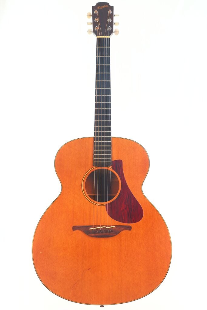 Die Lowden S-5 Akustik Gitarre hat eine natürliche Holzoberfläche, ein dunkles Griffbrett und ein rötlich-braunes Schlagbrett, das aufrecht vor einem schlichten weißen Hintergrund steht. Die Lowden S-5 Akustik Gitarre hat eine natürliche Holzoberfläche, ein dunkles Griffbrett und ein rötlich-braunes Schlagbrett, das aufrecht vor einem schlichten weißen Hintergrund steht.
