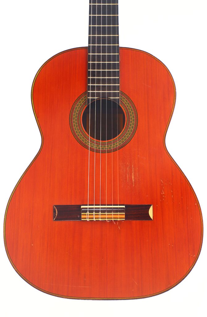 Die „Juan Estruch Chet Atkins Yellow Label 1976 Klassische Gitarre“ ist eine klassische Akustikgitarre mit einem rotbraunen Holzkorpus, sechs Saiten, einem runden Schallloch mit Ringen und einem dunklen Griffbrett, die hier isoliert auf weißem Hintergrund abgebildet ist. Die „Juan Estruch Chet Atkins Yellow Label 1976 Klassische Gitarre“ ist eine klassische Akustikgitarre mit einem rotbraunen Holzkorpus, sechs Saiten, einem runden Schallloch mit Ringen und einem dunklen Griffbrett, die hier isoliert auf weißem Hintergrund abgebildet ist.