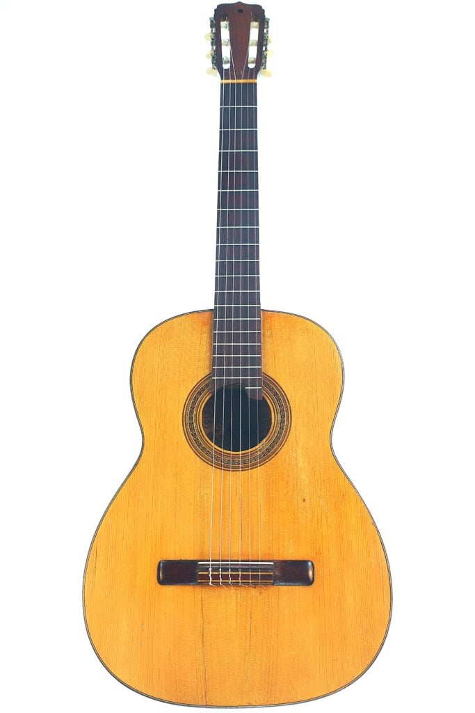 Die „Jose Ramirez I 1921 Klassische Gitarre“ ist eine klassische Akustikgitarre mit naturbelassener Holzoberfläche, sechs Saiten, einer Zierrosette, einem runden Schallloch und einem Sattel aus dunklem Holz, abgebildet vor weißem Hintergrund. Die „Jose Ramirez I 1921 Klassische Gitarre“ ist eine klassische Akustikgitarre mit naturbelassener Holzoberfläche, sechs Saiten, einer Zierrosette, einem runden Schallloch und einem Sattel aus dunklem Holz, abgebildet vor weißem Hintergrund.