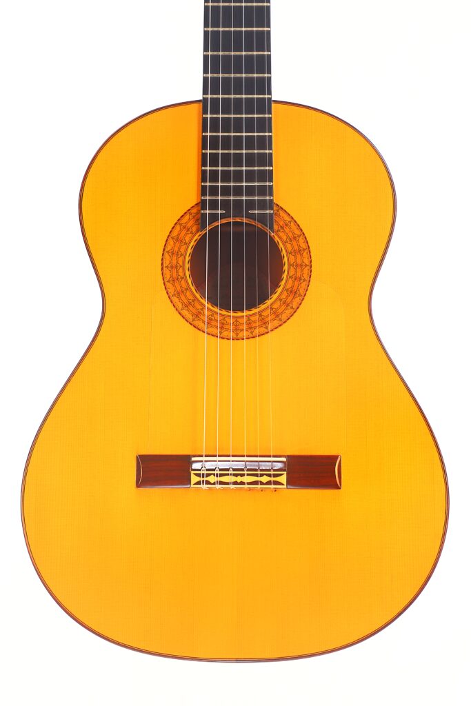 Die Juan Montero 1993 Blanca Flamenco Gitarre hat einen hellbraunen Holzkorpus, ein dunkles Griffbrett und eine dekorative Rosette um das Schallloch, die auf einem weißen Hintergrund abgebildet ist. Die Juan Montero 1993 Blanca Flamenco Gitarre hat einen hellbraunen Holzkorpus, ein dunkles Griffbrett und eine dekorative Rosette um das Schallloch, die auf einem weißen Hintergrund abgebildet ist.