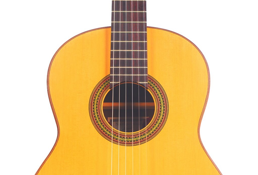 Nahaufnahme der klassischen Gitarre von Carl Hermann Schäfer – Nicolaus Wollf aus dem Jahr 2012, die ihre sechs Saiten, das verzierte Schallloch und die helle Holzoberfläche vor weißem Hintergrund hervorhebt. Nahaufnahme der klassischen Gitarre von Carl Hermann Schäfer – Nicolaus Wollf aus dem Jahr 2012, die ihre sechs Saiten, das verzierte Schallloch und die helle Holzoberfläche vor weißem Hintergrund hervorhebt.