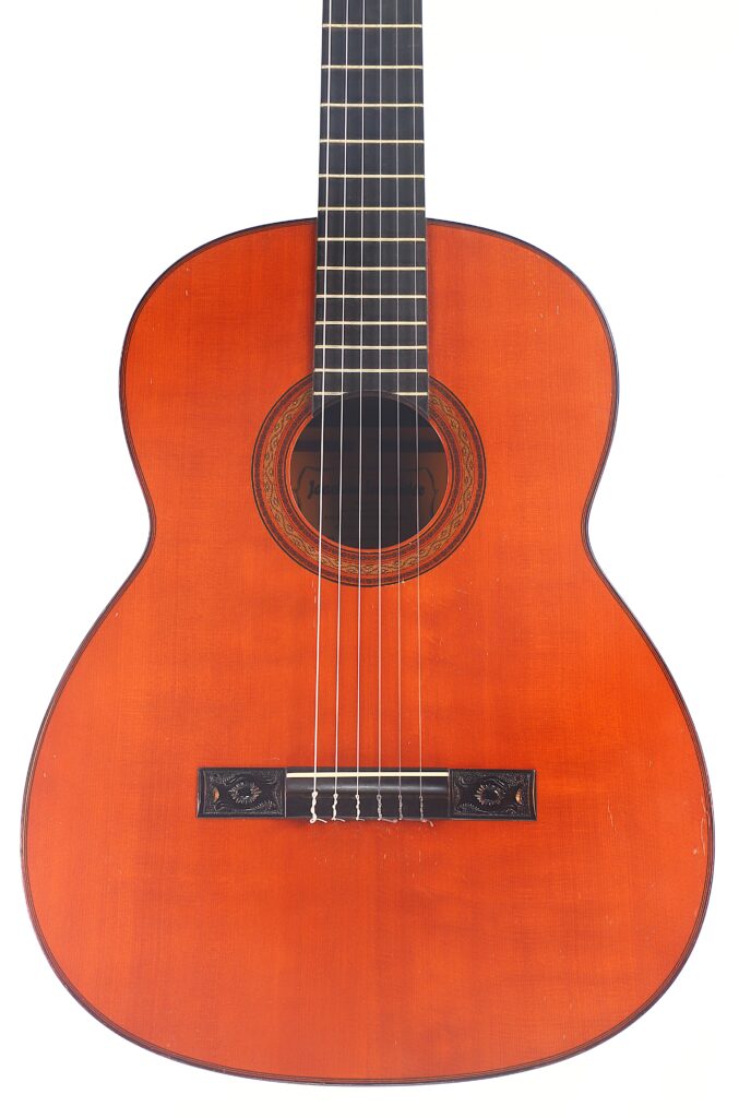 Die „Joachim Schneider 1977 Klassische Gitarre“ verfügt über einen rotbraunen Holzkorpus, ein schwarzes Griffbrett, eine verzierte Rosette um das Schallloch sowie sechs Saiten, die vor einem weißen Hintergrund zu sehen sind. Die „Joachim Schneider 1977 Klassische Gitarre“ verfügt über einen rotbraunen Holzkorpus, ein schwarzes Griffbrett, eine verzierte Rosette um das Schallloch sowie sechs Saiten, die vor einem weißen Hintergrund zu sehen sind.