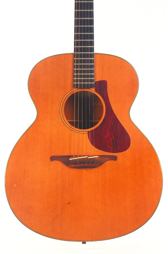 Die Lowden S-5 Akustik-Gitarre hat ein natürliches Holzfinish, ein dunkles Griffbrett und ein rotbraunes Schlagbrett, das vor einem weißen Hintergrund abgebildet ist. Die Lowden S-5 Akustik-Gitarre hat ein natürliches Holzfinish, ein dunkles Griffbrett und ein rotbraunes Schlagbrett, das vor einem weißen Hintergrund abgebildet ist.